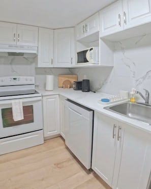 A kitchen with white cabinets, a built-in oven, a microwave, a sink, and a coffee maker. - Modern Delson Home South Shore Montreal (Delson)