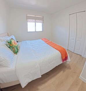 A bedroom with a bed, a window with blinds, and a white door. - Modern Delson Home South Shore Montreal (Delson)