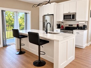 Una cocina moderna con armarios blancos, un refrigerador de acero inoxidable, un microondas y una cafetera. Hay dos taburetes negros en la isla.