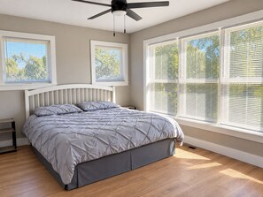 Een slaapkamer met een bed, een plafondventilator en grote ramen met zonwering.