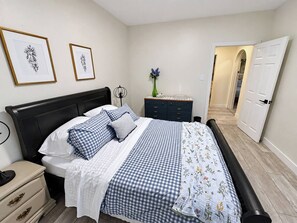 Een slaapkamer met een bed, nachtkastjes, een kaptafel, lijstwerken aan de muur en een deur die naar een andere kamer leidt.