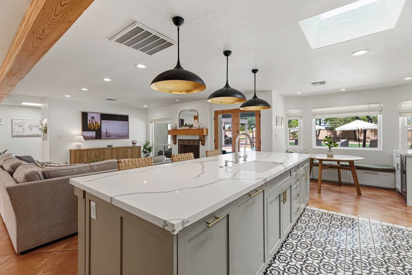A modern kitchen with a central island, pendant lights, and a view to the outside.