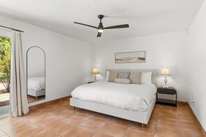 Ein Schlafzimmer mit einem Bett, zwei Nachttischen mit Lampen, einem Deckenventilator und einem Fenster mit Vorhängen.