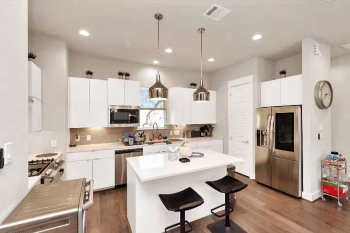 A modern kitchen with white cabinets, stainless steel appliances, a central island with bar stools, and pendant lighting.