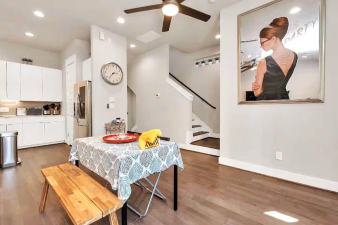 Una cocina moderna con armarios blancos, una mesa de comedor con mantel estampado y un banco de madera.