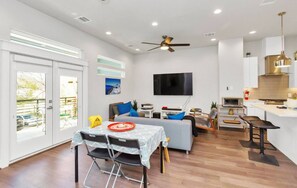 A modern living room with a sofa, TV, and dining area with chairs and a table. - Tx Home Group in Houston (Houston)