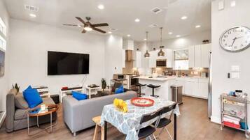 A modern apartment with a living room, dining area, kitchen, and a large TV.