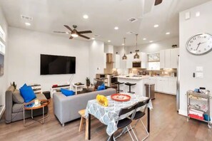A modern apartment with a living room, dining area, kitchen, and a large TV. - Tx Home Group in Houston (Houston)