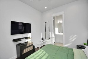 A modern bedroom with a bed, a TV mounted on the wall, a desk, and a walk-in closet. - Tx Home Group in Houston (Houston)
