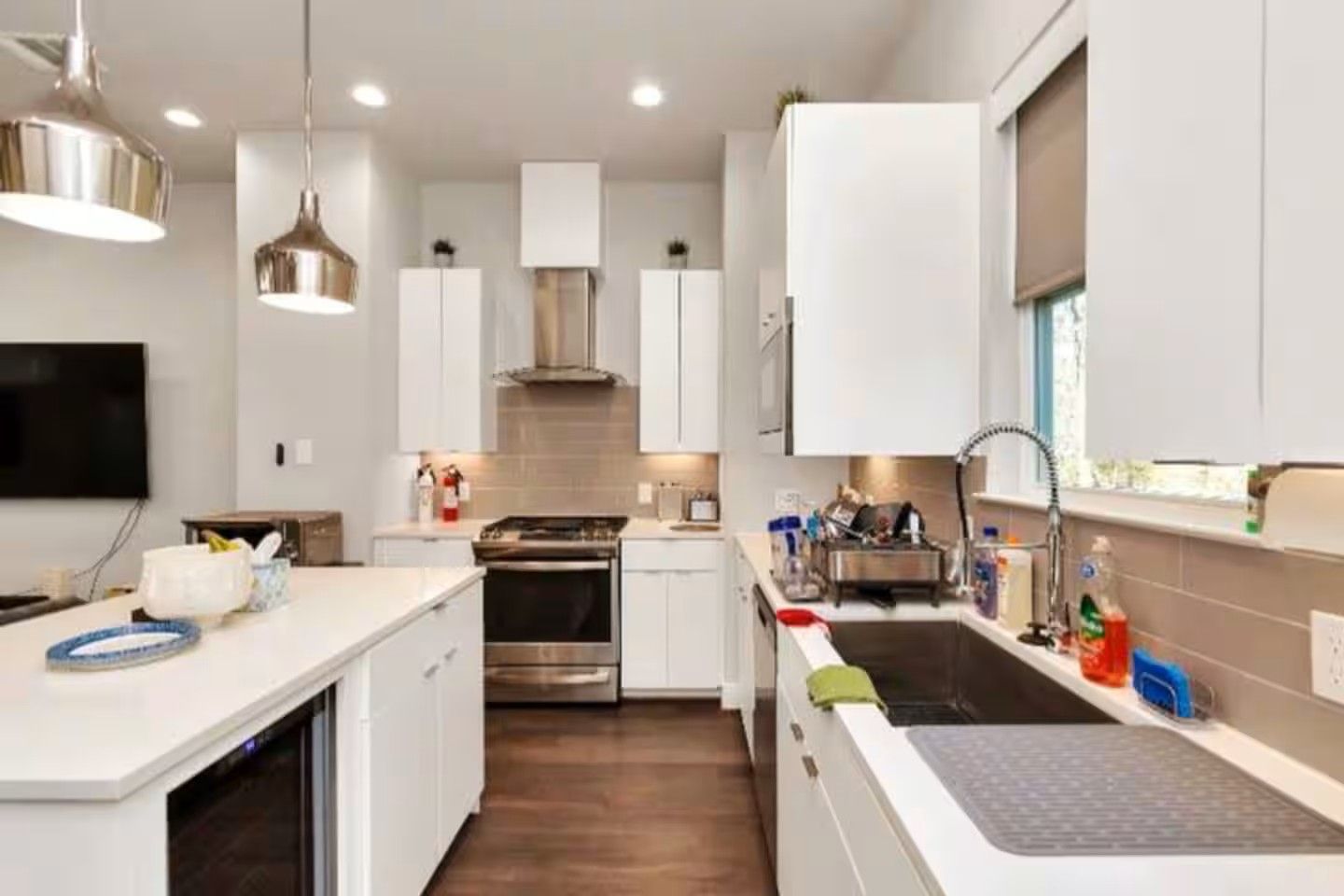 A modern kitchen with white cabinetry, stainless steel appliances, and pendant lighting.