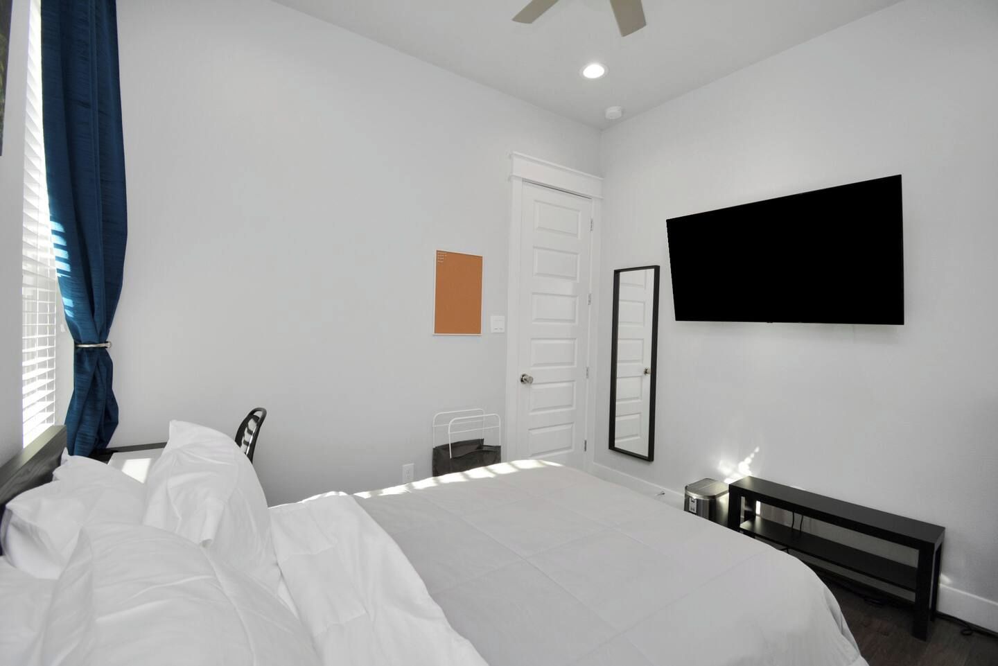 A bedroom with a bed, a desk, a chair, a TV, and a door.