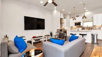 A modern living room with a grey sofa, blue cushions, a coffee table, and a flat-screen TV mounted on the wall.