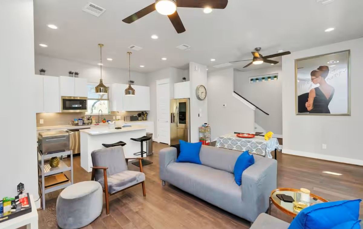 Una sala moderna con un sofá gris, una mesa de centro y un comedor, con una cocina al fondo.