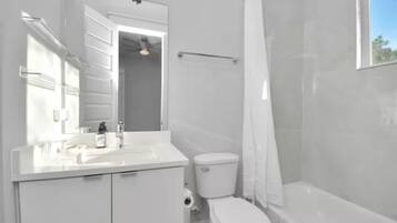 A modern bathroom with a white vanity, toilet, and bathtub.