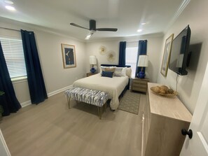 A bedroom with a bed, bedside tables, a ceiling fan, a wall-mounted TV, and a window with curtains. - Houston Haven Spacious 3BR Near Downtown (Houston)
