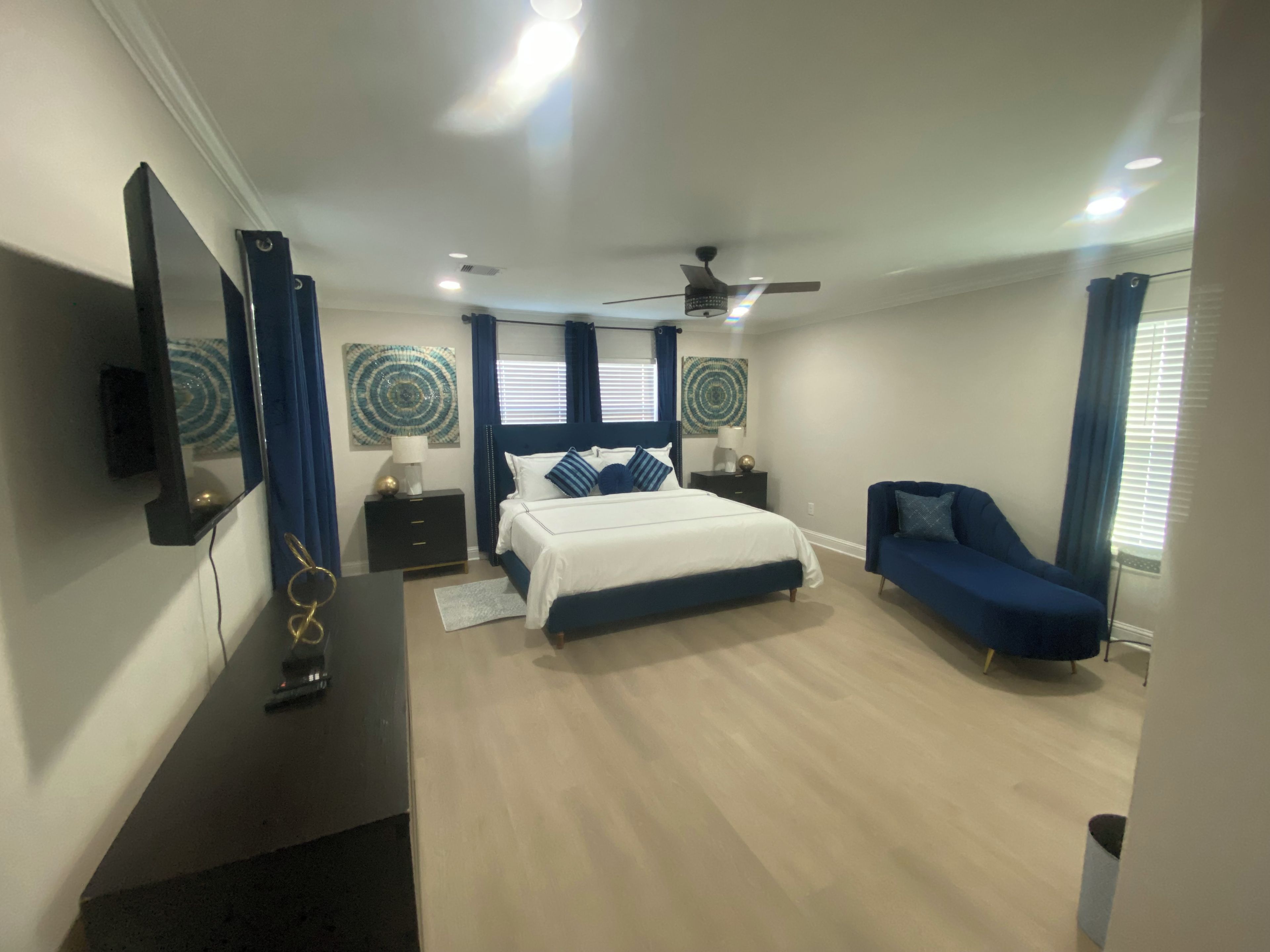 A bedroom with a bed, a desk, a chair, a ceiling fan, and artwork on the walls.