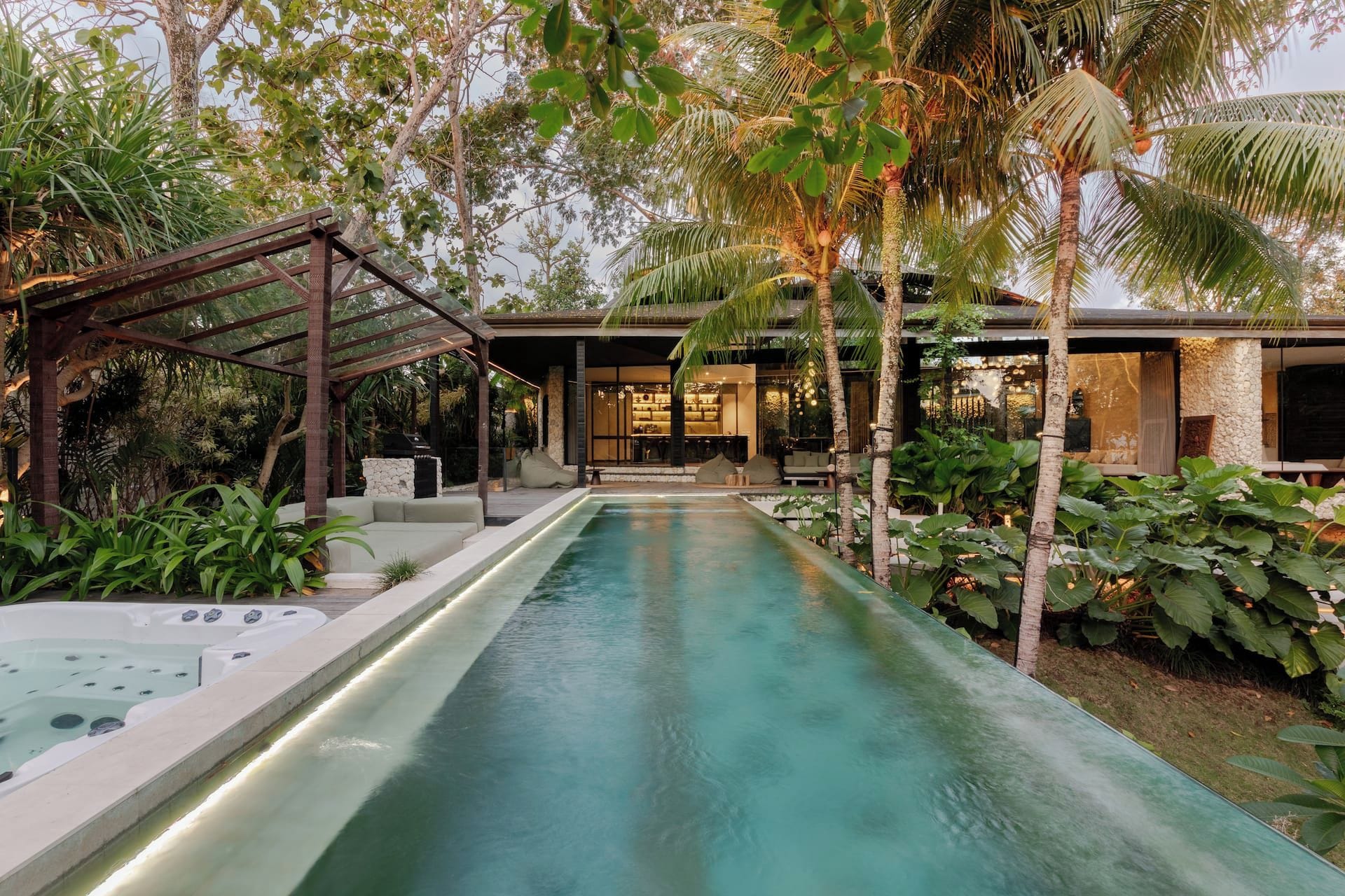 Un área de piscina moderna al aire libre con un jacuzzi, rodeada de exuberante vegetación tropical y palmeras.