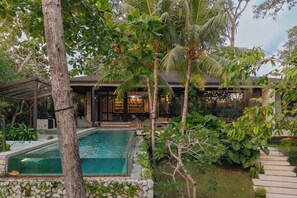 Une maison moderne dotée d’une piscine, entourée d’une végétation luxuriante et agrémentée d’une terrasse en bois.