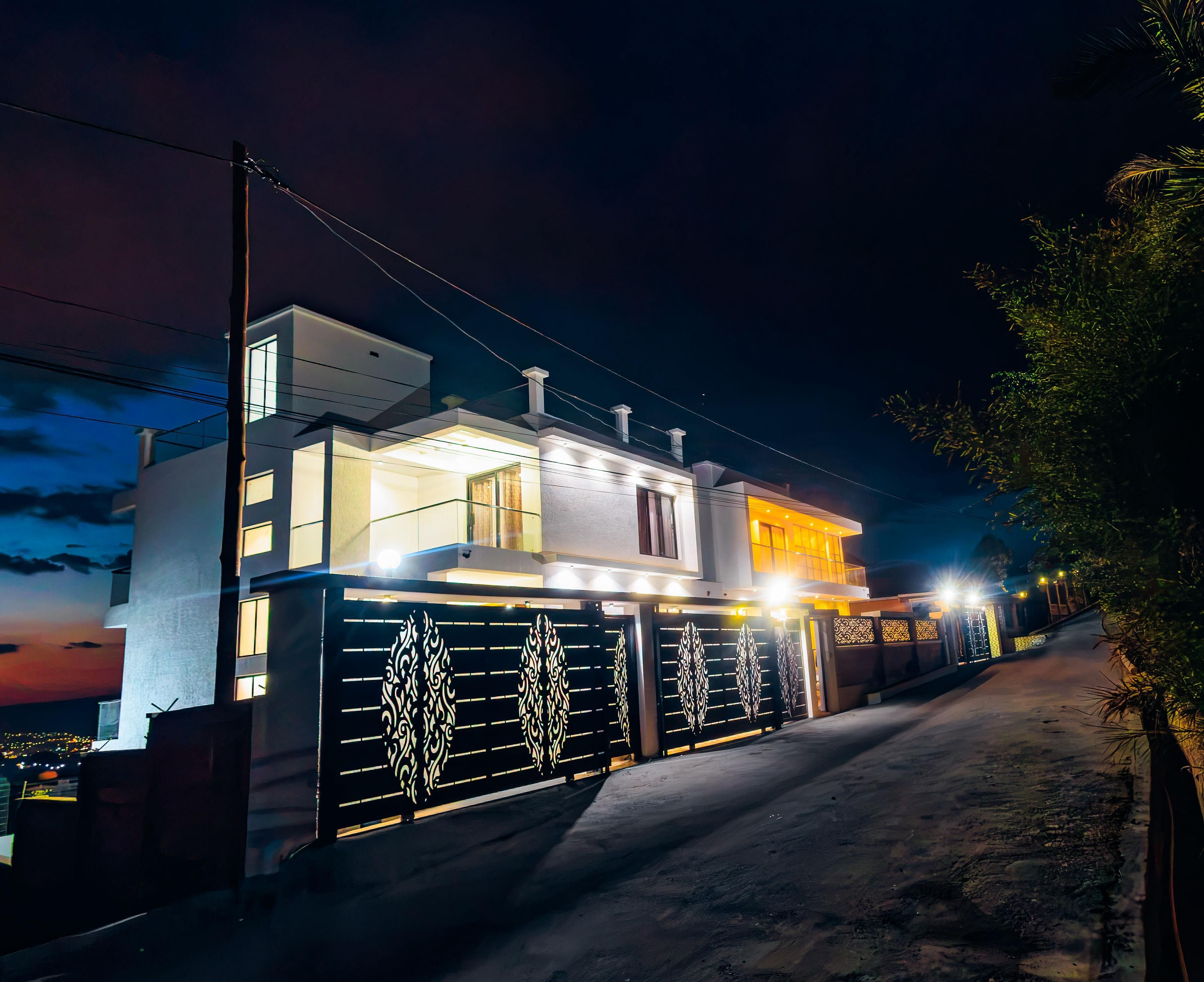 Una casa moderna de dos pisos con entrada protegida por un portón, un balcón visible y un camino de acceso a la vivienda.