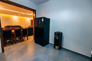 A compact kitchen with a refrigerator, a water dispenser, and a dining area with chairs and a table. - CRYSTAL APARTMENT AND GUEST HOUSE (Kigali)