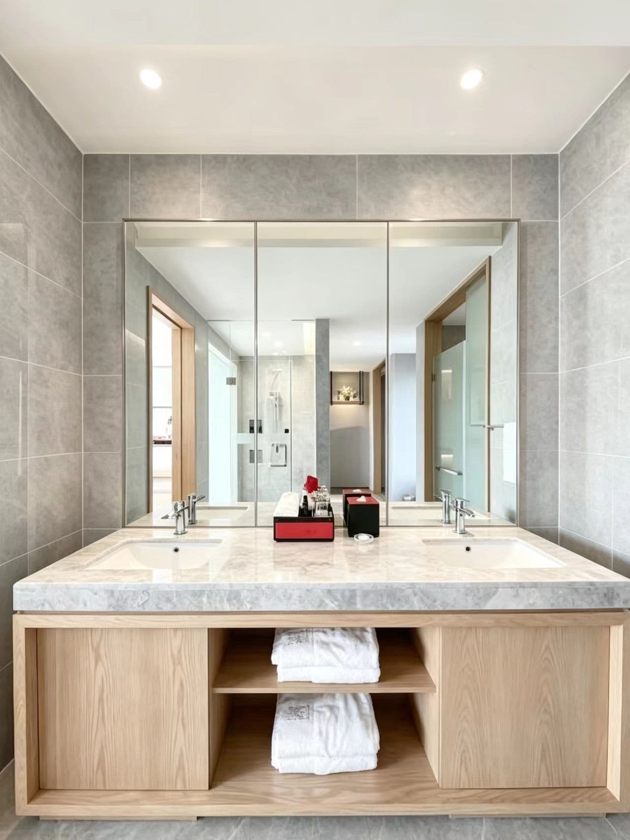 Un bagno moderno con uno specchio grande, due lavandini e un mobile bagno in legno con spazio contenitore.