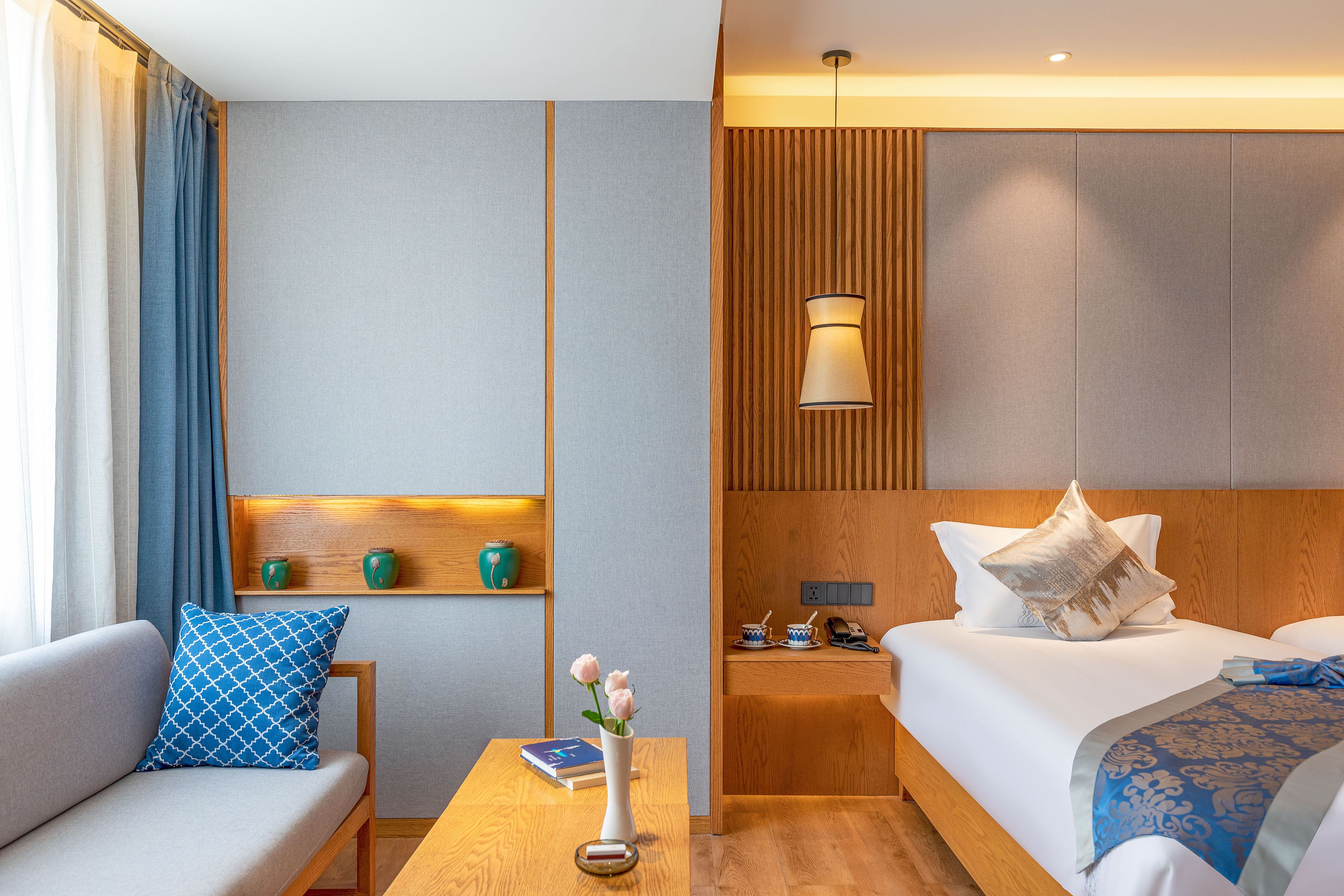 Quarto de hotel com sofá, mesa de cabeceira com um vaso de flores, cama com travesseiros e criado-mudo com abajur.