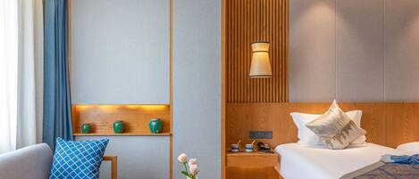 Quarto de hotel com sofá, mesa de cabeceira com um vaso de flores, cama com travesseiros e criado-mudo com abajur.