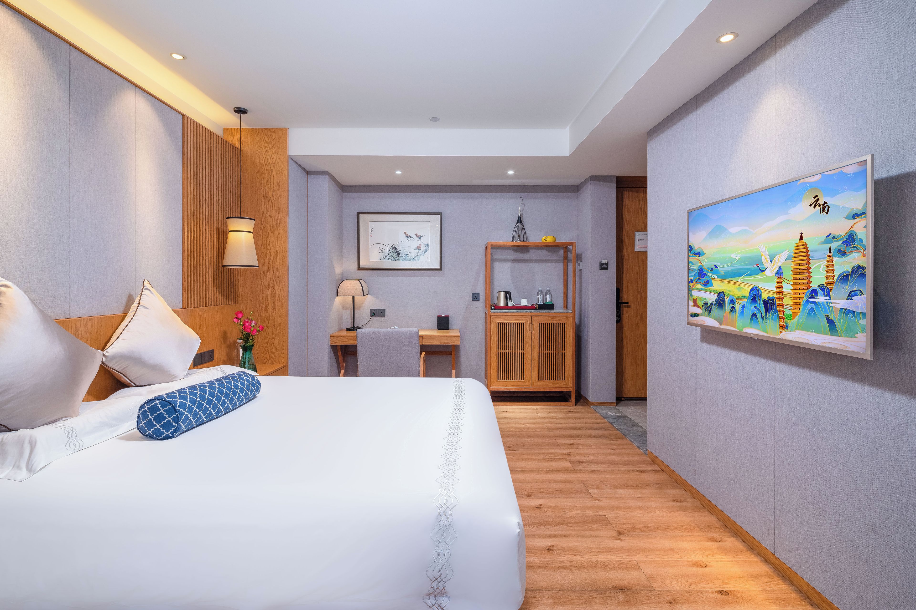 A hotel room with a bed, a desk, a chair, a cabinet, and a painting on the wall.