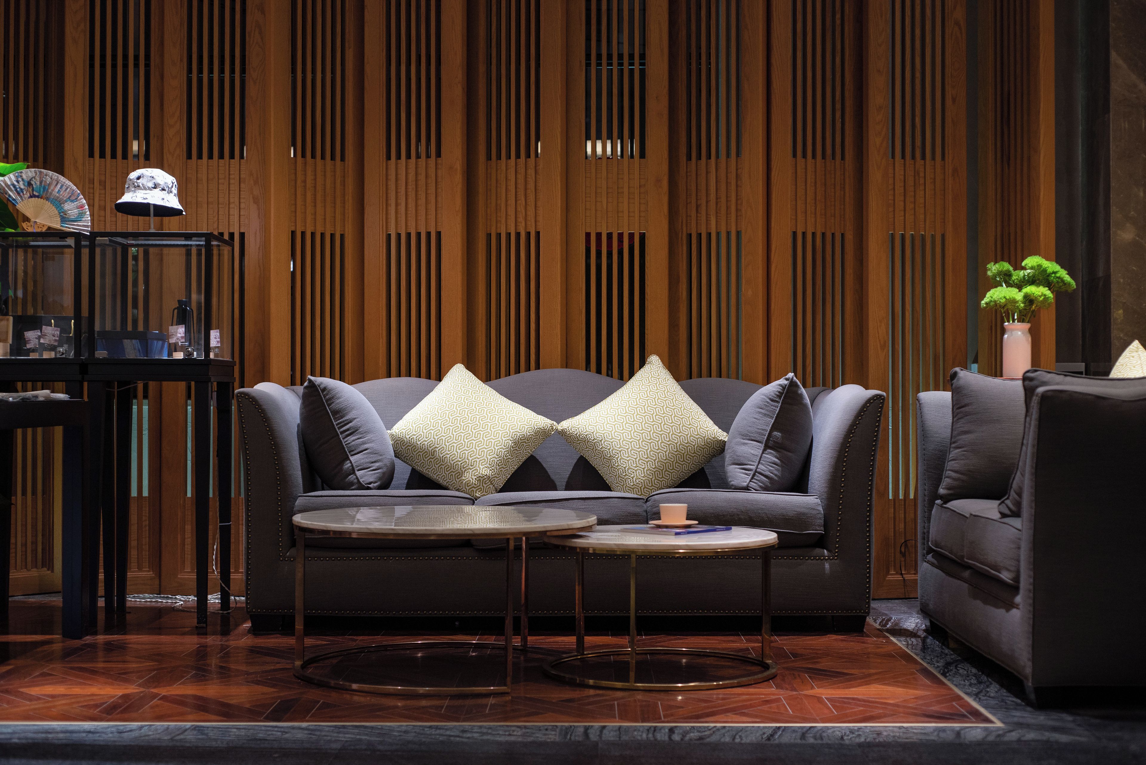 A modern living room with a dark grey sofa, two patterned throw pillows, a small round coffee table, and a wooden slatted wall in the background.