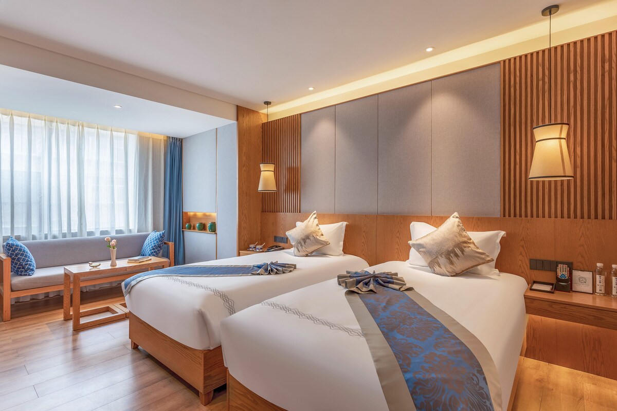 A hotel room with two beds, a sofa, a small table, and a nightstand.