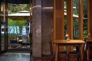 A wooden table with a vase of flowers, a chair, and a view of outdoor seating with umbrellas.
