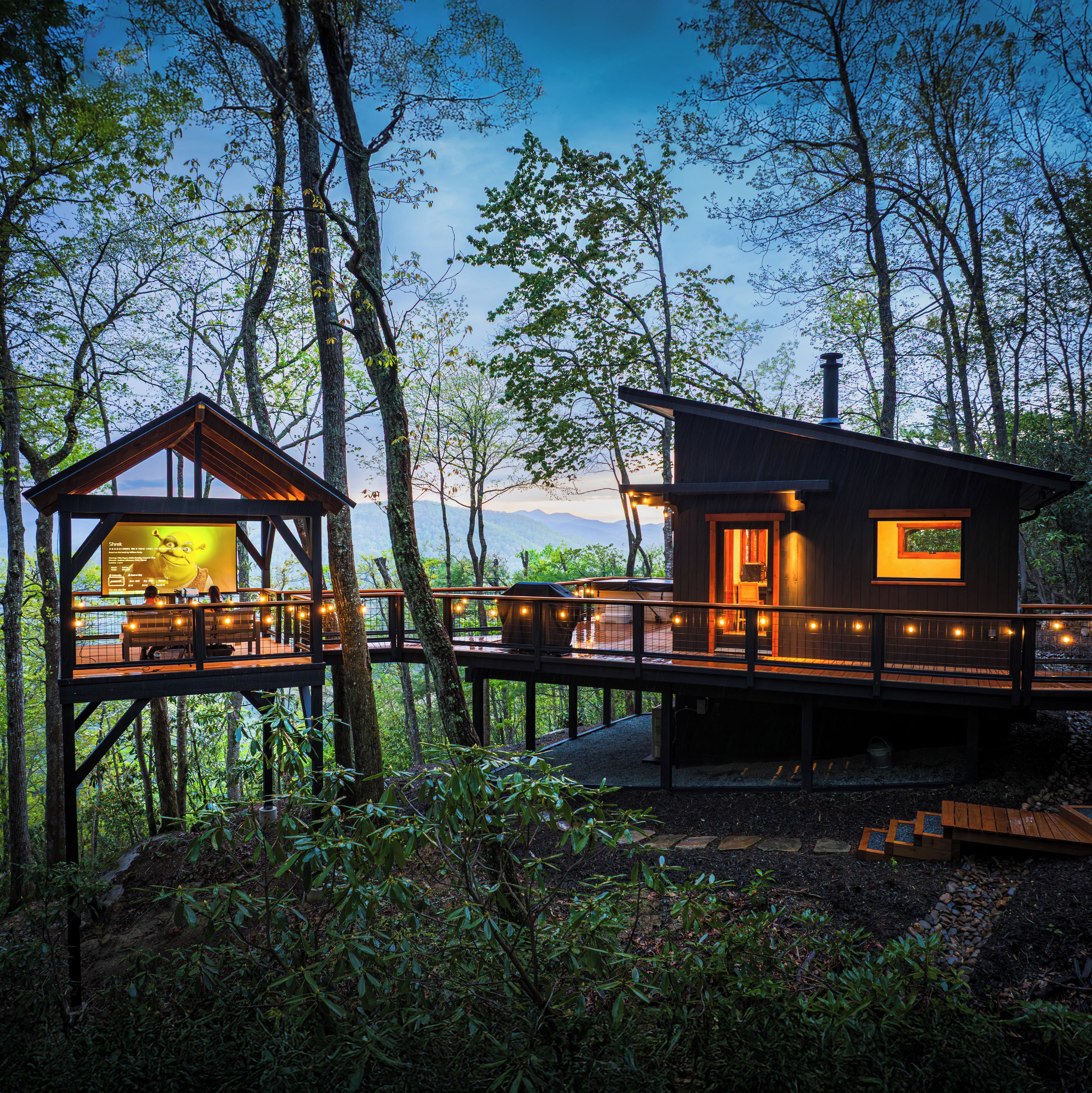 A cabin with a deck and a separate wooden structure, surrounded by trees.
