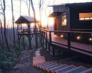 A wooden cabin with a deck and a covered area, surrounded by trees.