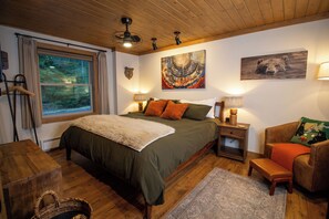 Een slaapkamer met een groot bed, een raam met uitzicht op bomen, een houten plafond en een berenbeeld.