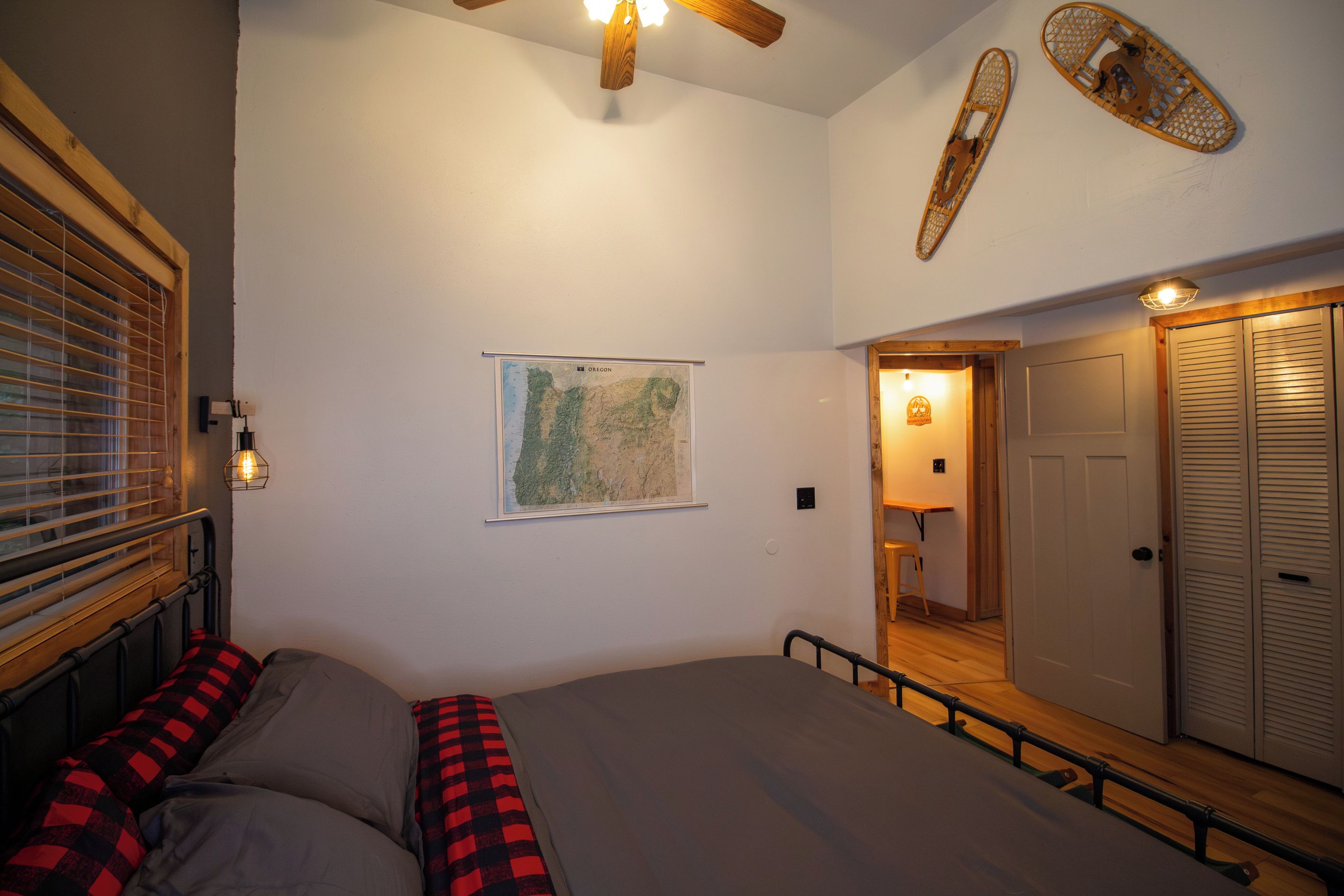 A bedroom with a bed, a map on the wall, a wooden ceiling fan, and a door with louvered shutters.