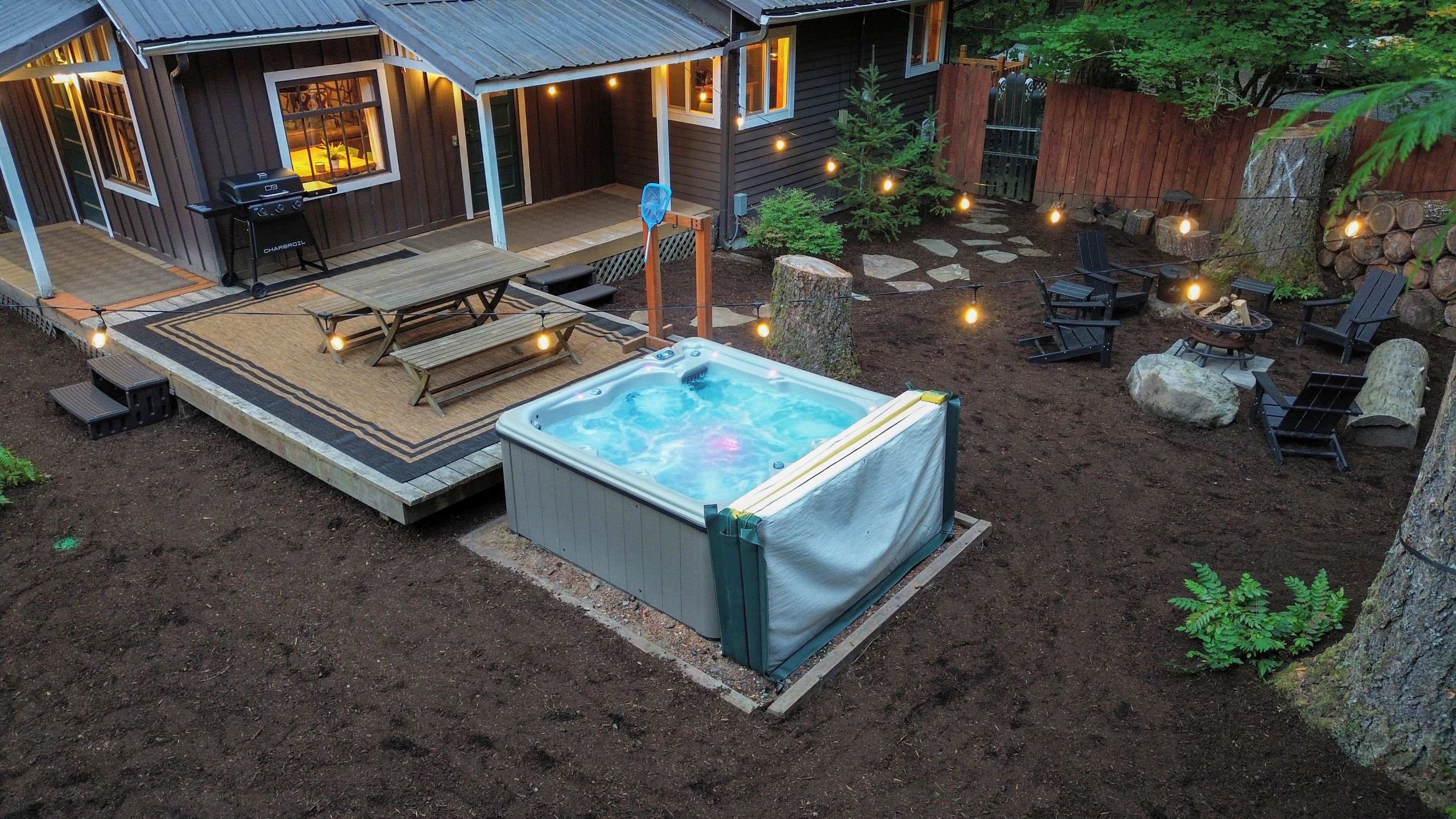 Un jardin avec un jacuzzi, une terrasse en bois, un coin salon extérieur et un foyer.