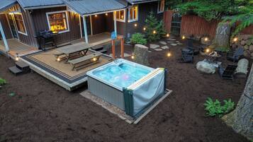Un jardin avec un jacuzzi, une terrasse en bois, un coin salon extérieur et un foyer.
