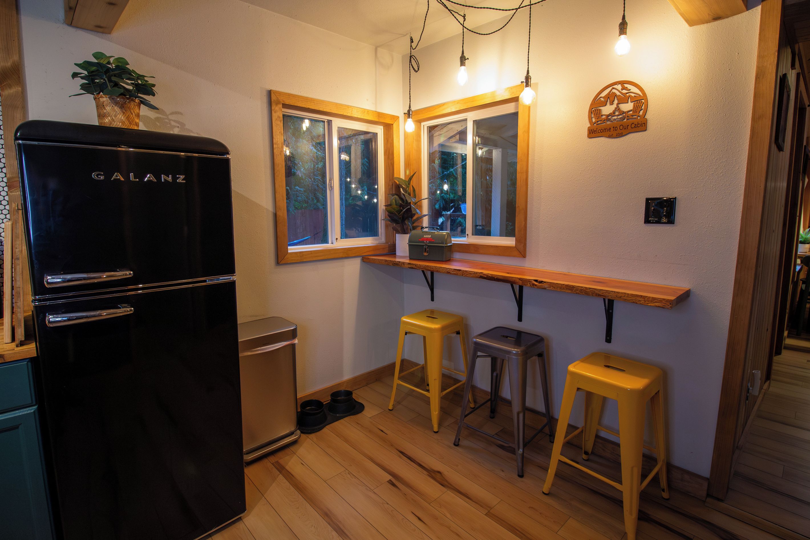 A compact kitchen with a Galanz refrigerator, wooden flooring, and two yellow stools.