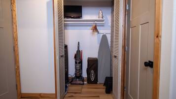 A narrow hallway with a wooden floor, a television mounted on a wall, a vacuum cleaner, and a folding ironing board.