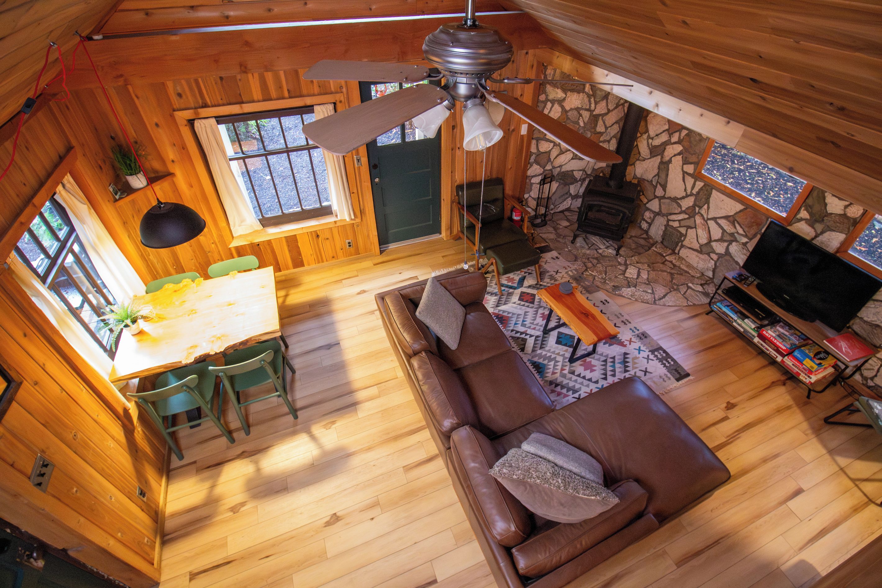 A cozy cabin interior with a dining area, a living room with a sofa, and a stone fireplace.