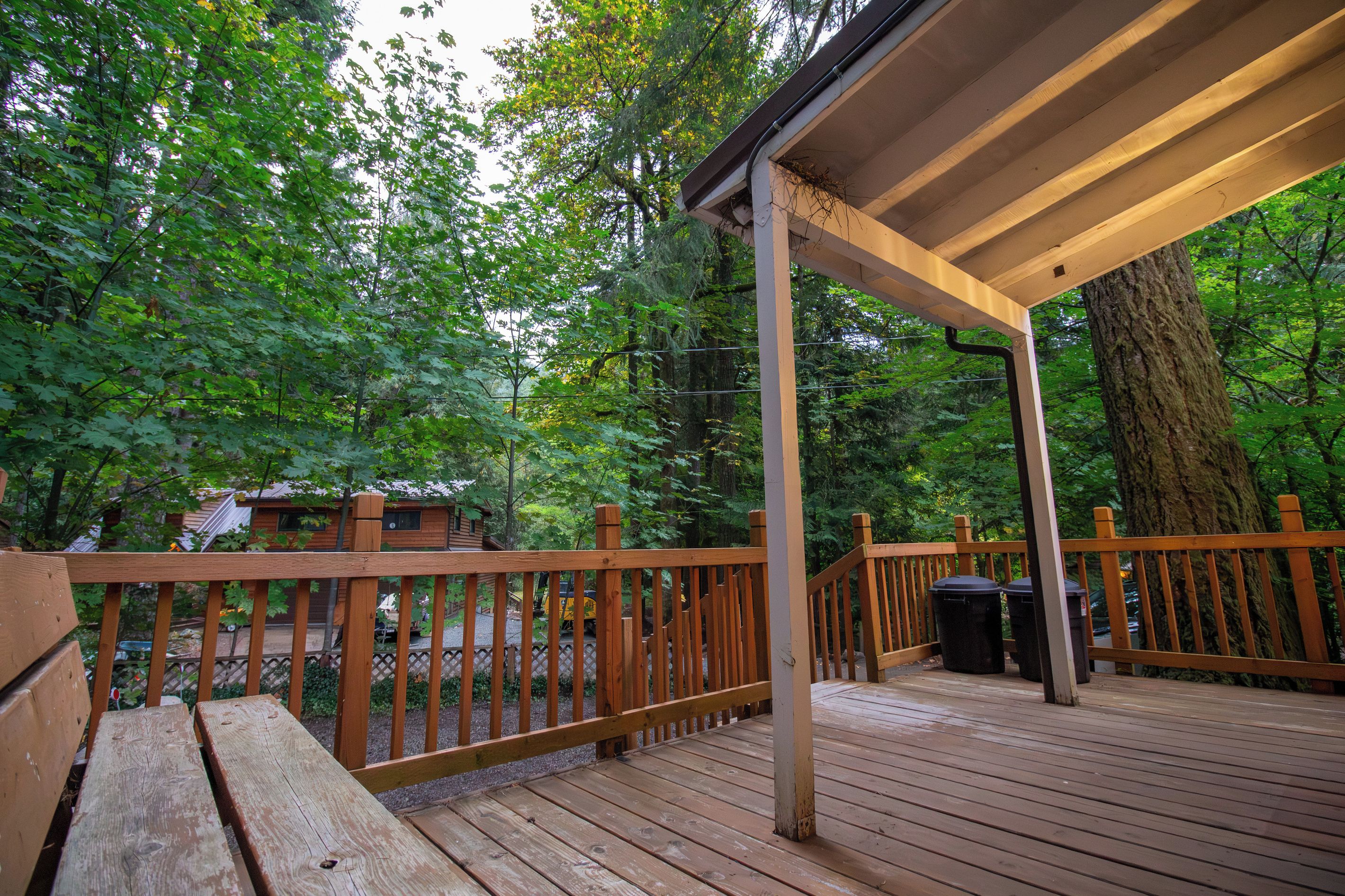 A wooden deck with a railing, surrounded by trees and a covered area.