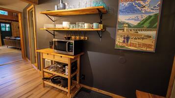 A kitchen with wooden shelves holding dishes and glasses, a microwave, and a poster of Bonneville Dam.