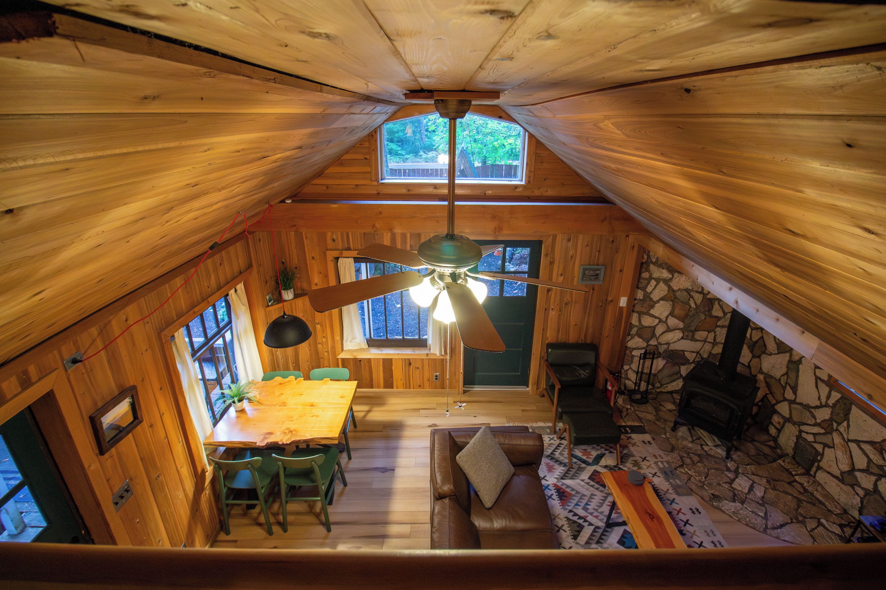 A cabin interior with a dining area, a fireplace, and a loft space.