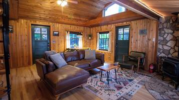 A cozy cabin interior with a leather sofa, a dining table, and a fireplace.