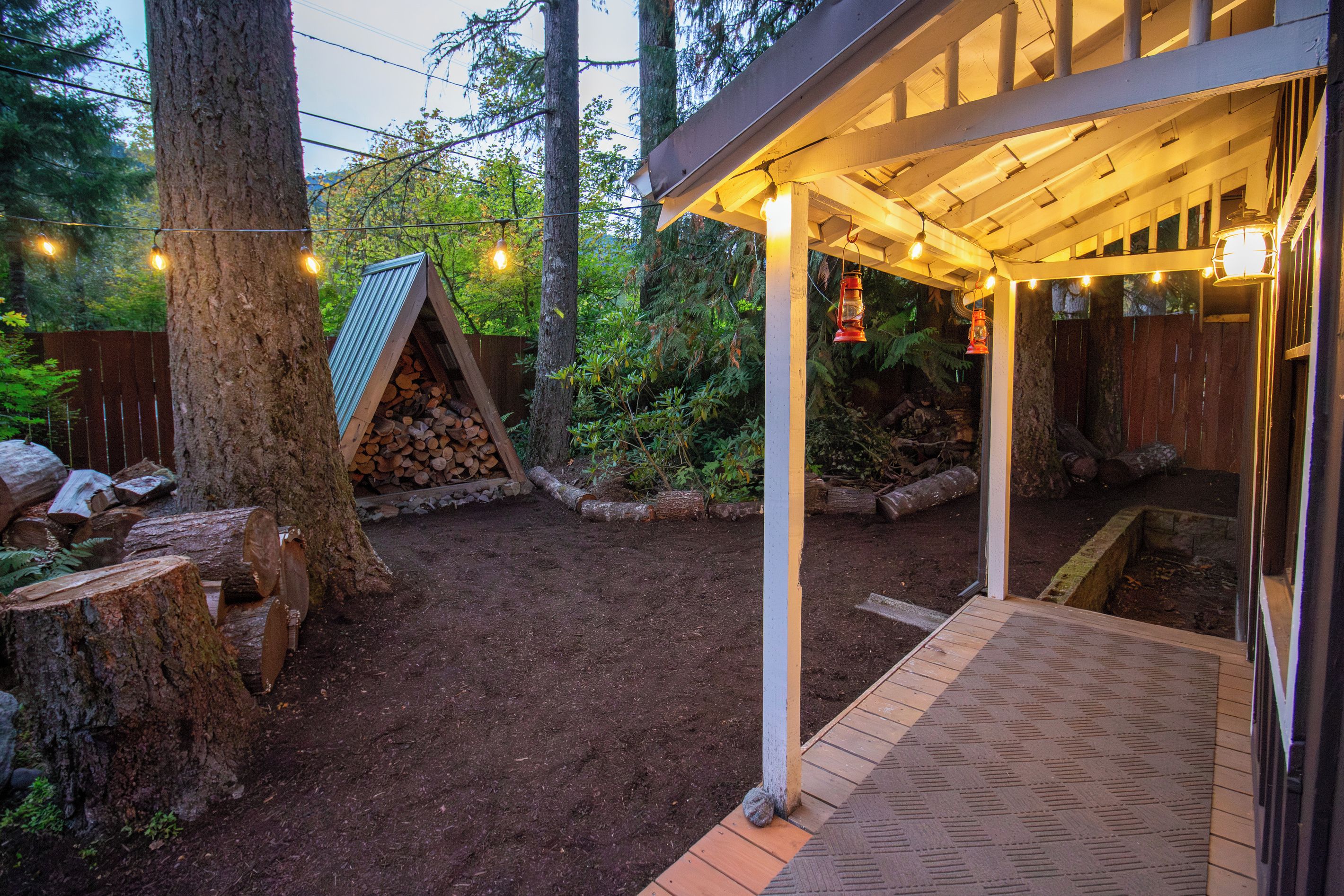 Un espacio al aire libre techado con cubierta de madera, leña apilada y estructura de techo metálico.