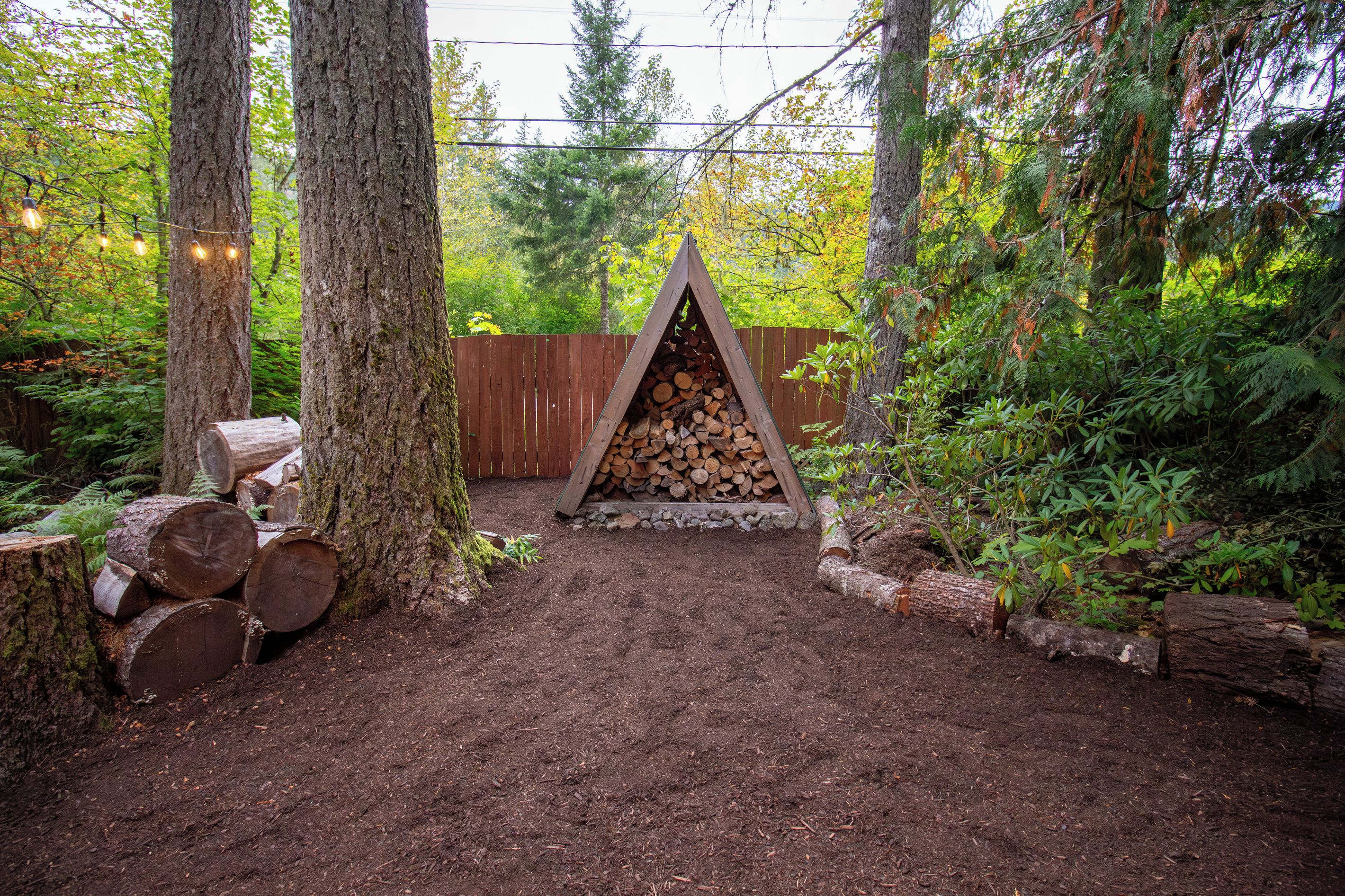 A forested area with a pile of logs and a wooden fence.