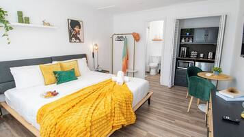 Ein modernes Hotelzimmer mit Bett, Nachttisch und Blick in den Küchenbereich.