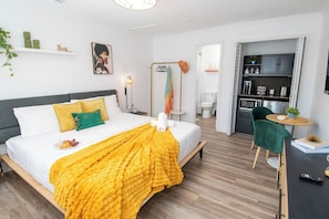 Una habitación de hotel moderna con cama, mesita de noche y vista hacia la zona de la cocina.