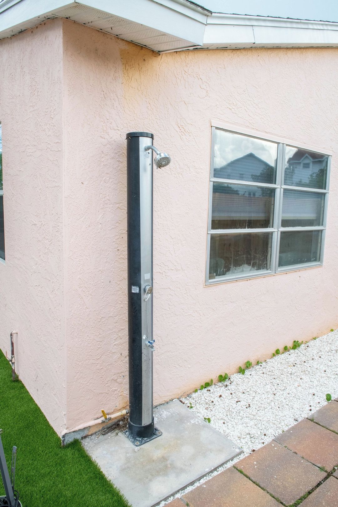 A building corner with a metal structure, a window, and a small patch of grass.