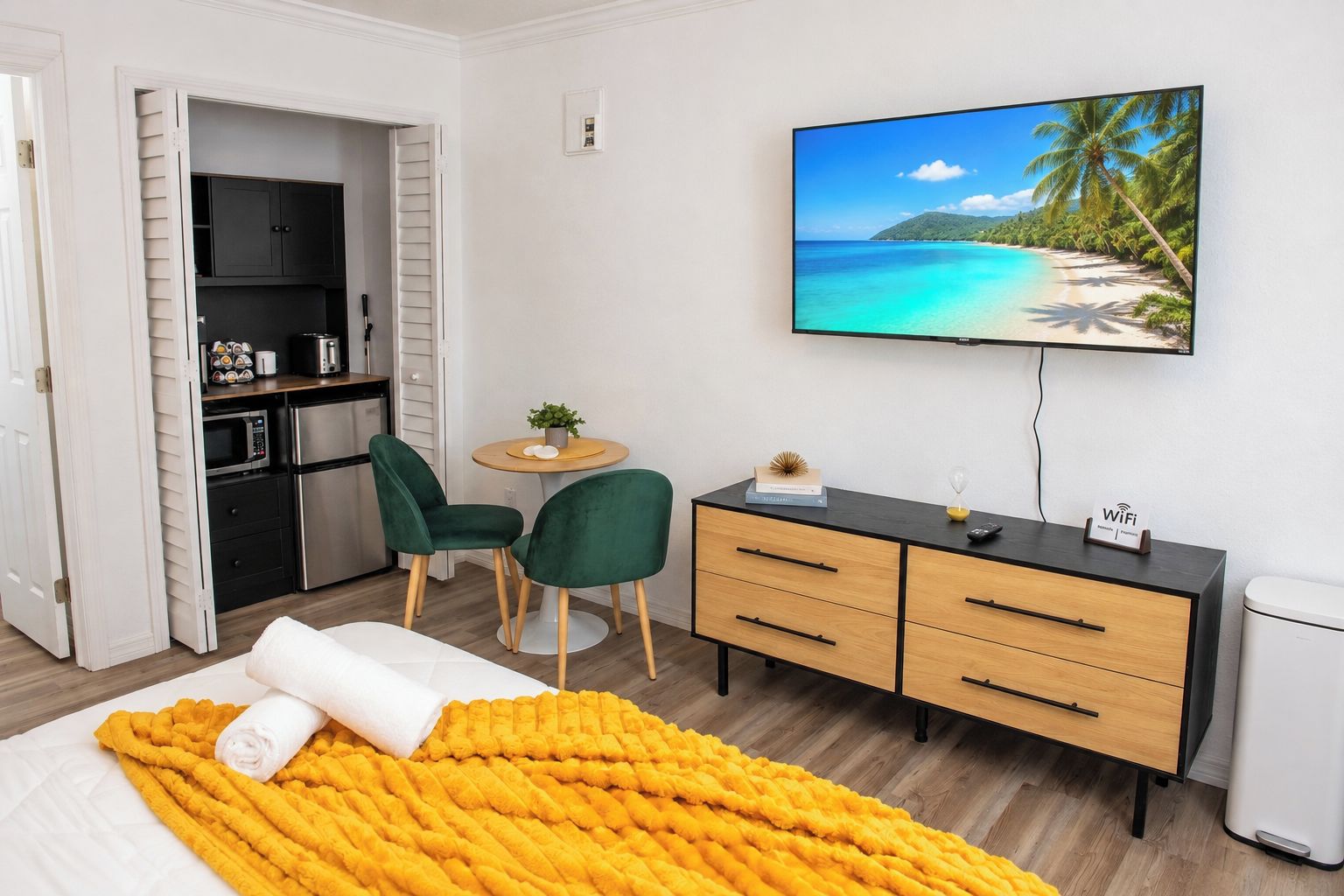 A hotel room with a bed, a desk, a TV, and a kitchenette.